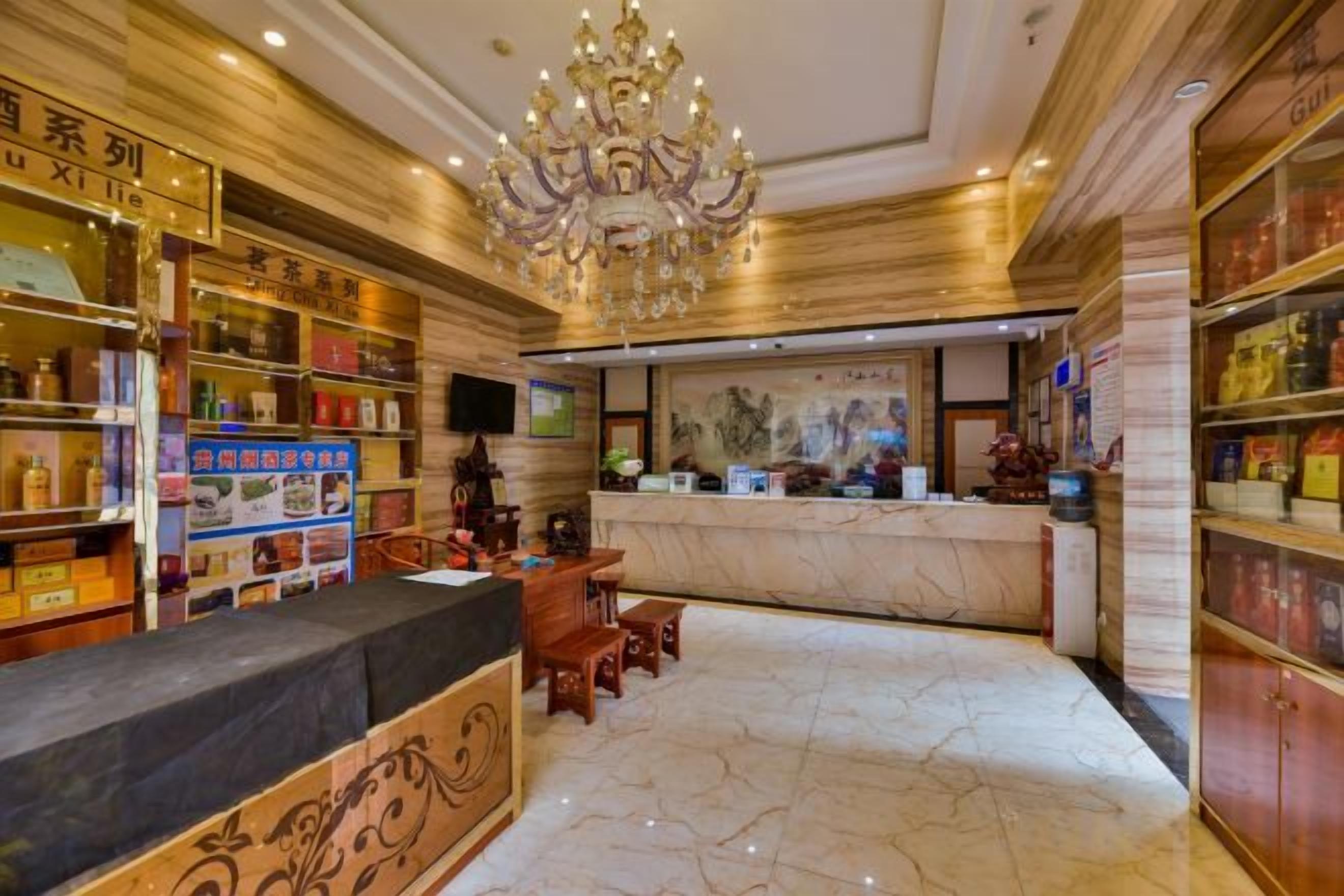 A hotel lobby with a reception desk, a chandelier, and shelves with various items.