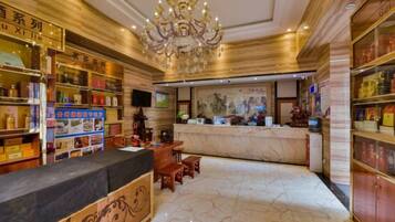 A hotel lobby with a reception desk, a chandelier, and shelves with various items.
