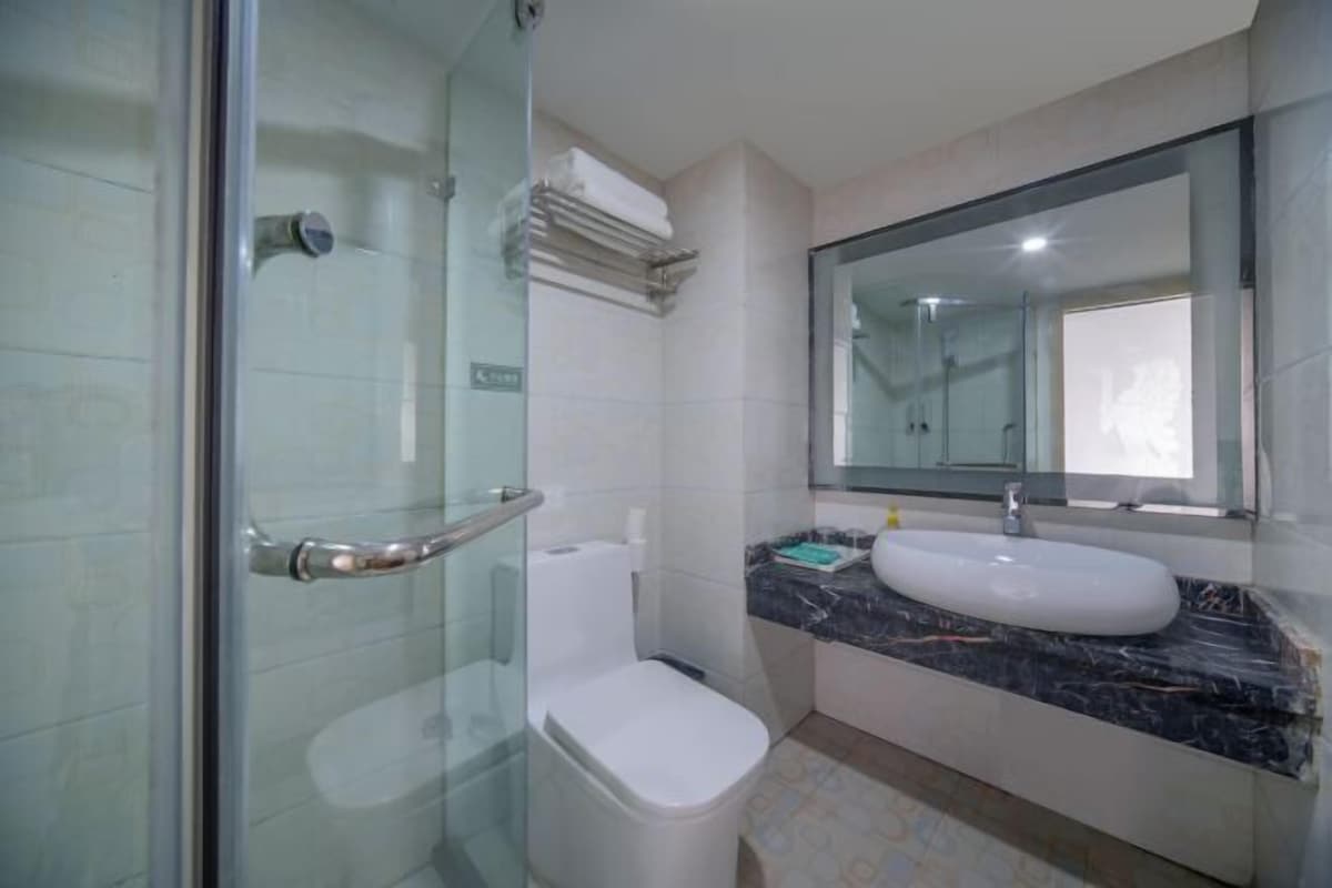 A bathroom with a glass shower enclosure, a white toilet, a marble countertop, and a large mirror.