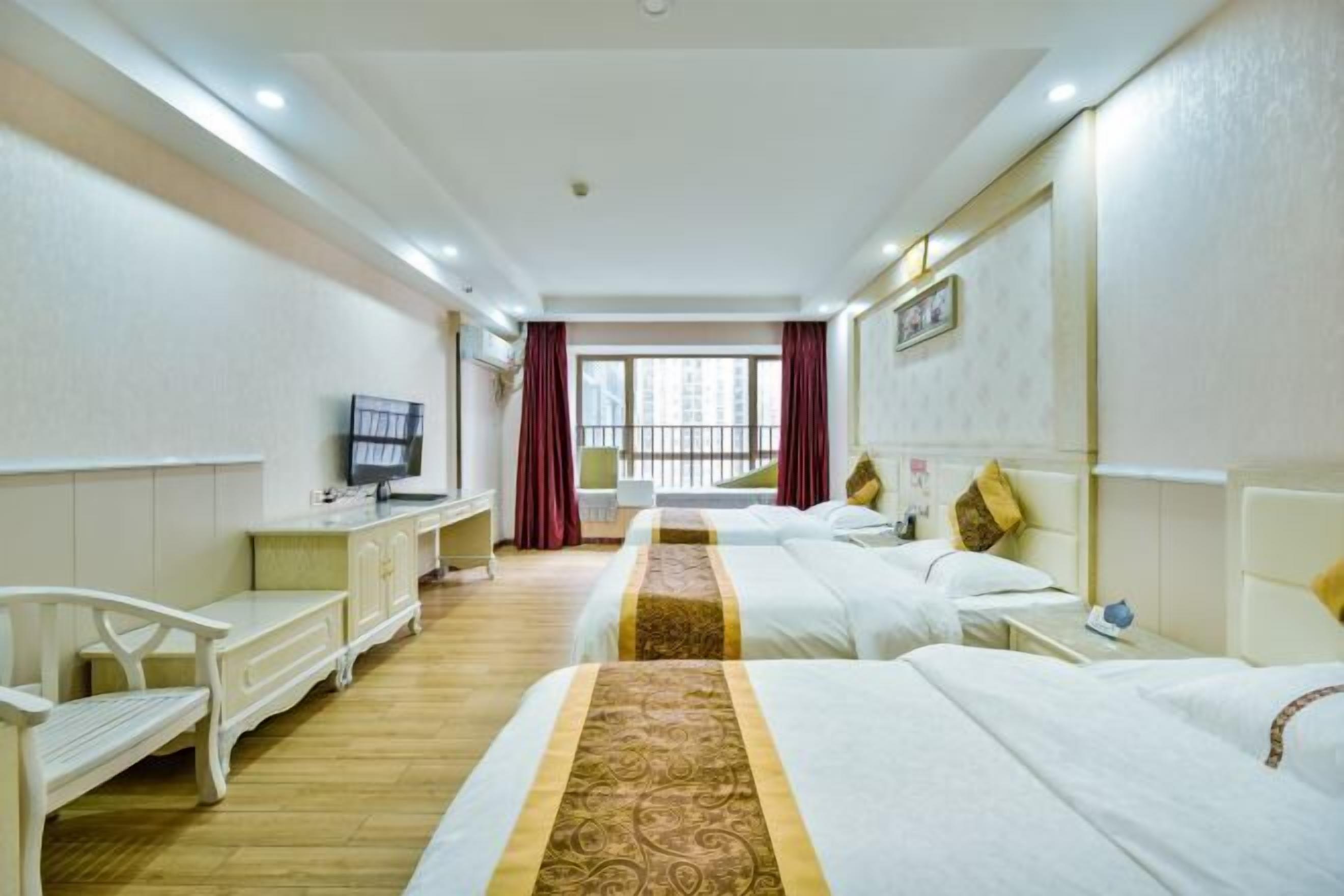 A hotel room with two beds, a TV, a desk, and a window with curtains.