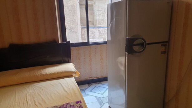 Quarto com cama, geladeira e janela com persianas.