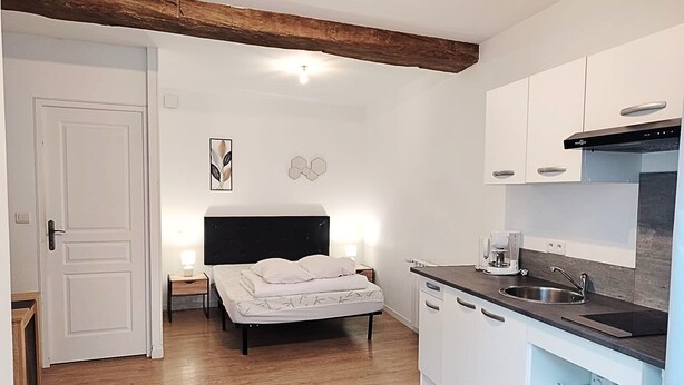 Ein kleines Hotelzimmer mit Bett, Nachttisch und einer Küchenzeile.