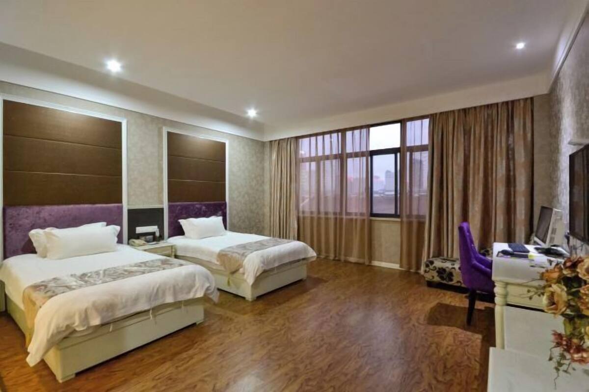 A hotel room with two beds, a desk with a computer, and a large window with curtains.