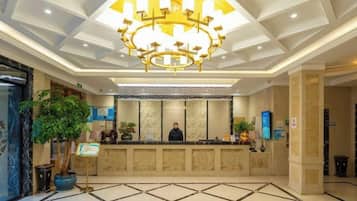 A hotel reception area with a large chandelier, a reception desk, and a potted plant.