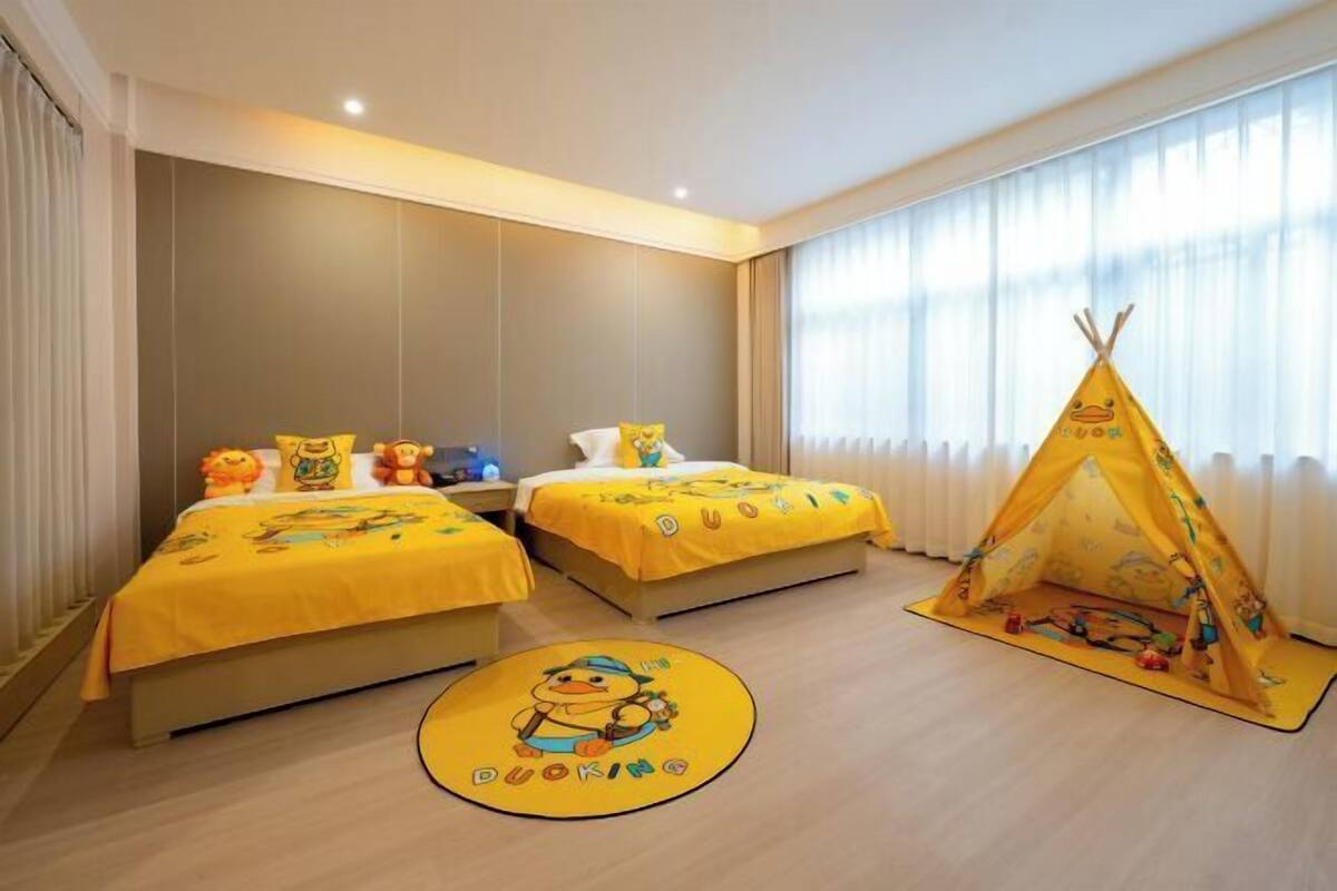 A hotel room with two beds, a yellow play tent, and a round rug with a duck design.