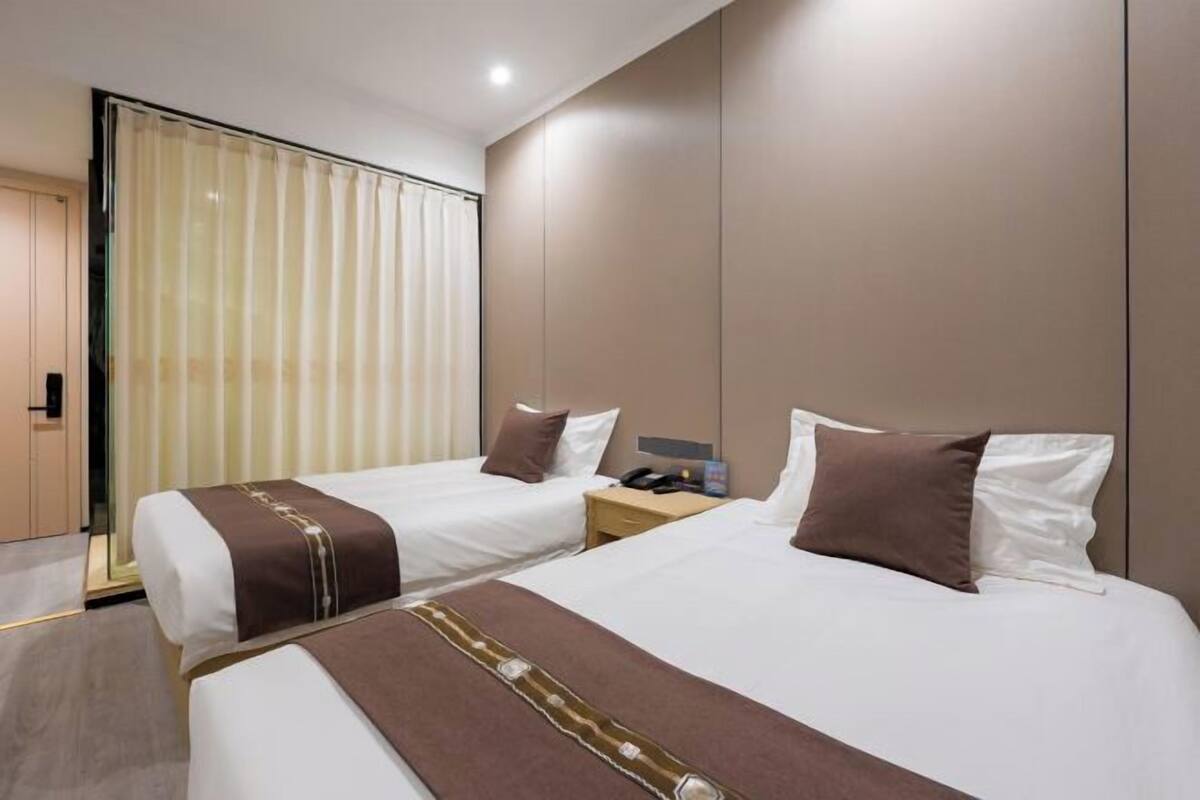 A hotel room with two beds, a bedside table with a phone, and a window with blinds.