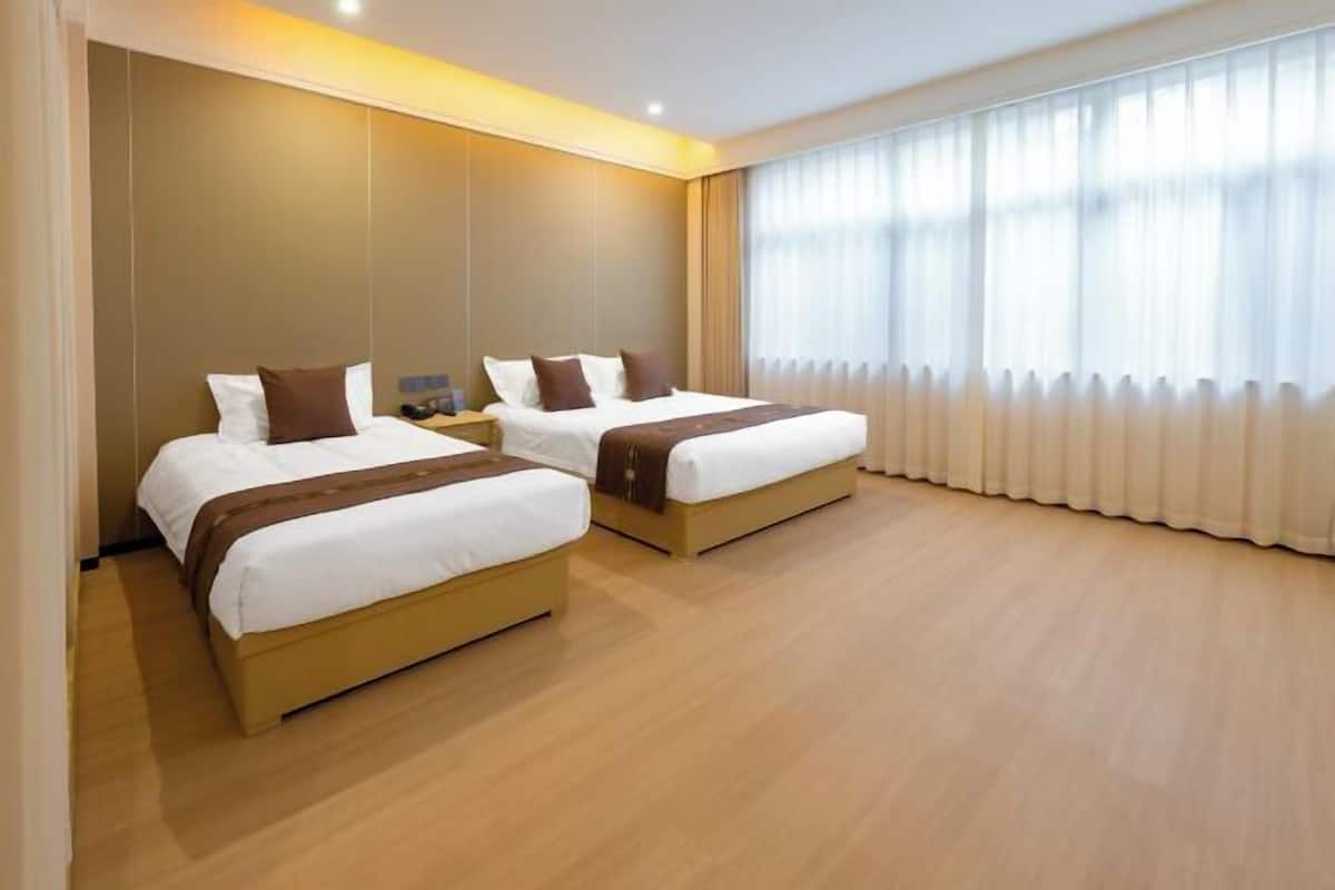 A hotel room with two beds, a wooden floor, and a large window with curtains.