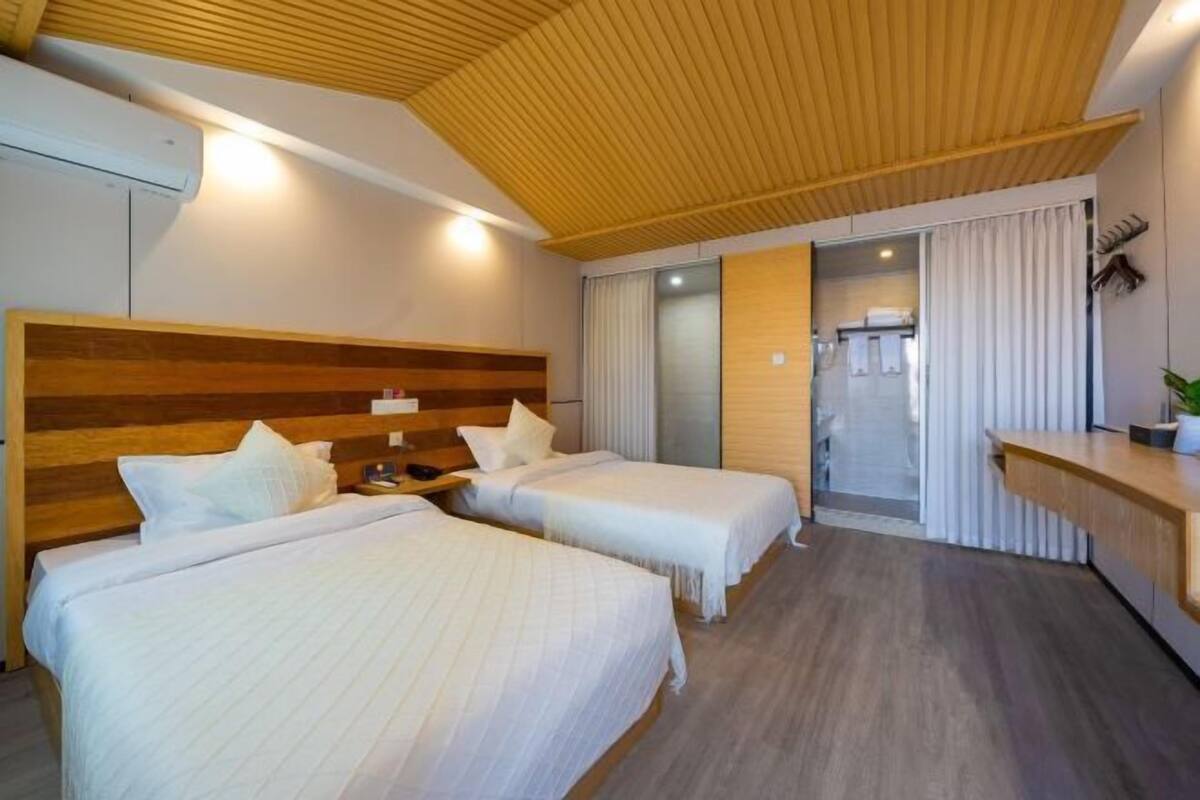 A hotel room with two beds, wooden headboard, a desk, and a sliding door leading to a bathroom.