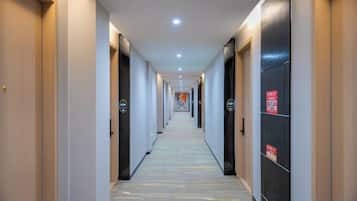 Un pasillo de hotel con puertas a ambos lados, piso cubierto de alfombra e iluminación en el techo.