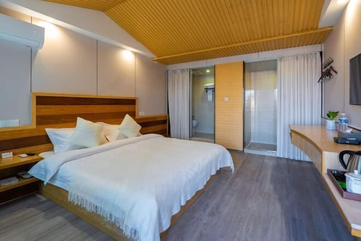 A hotel room with a wooden headboard, a bed with white bedding, a bedside table with a lamp, and a sliding glass door leading to a balcony.