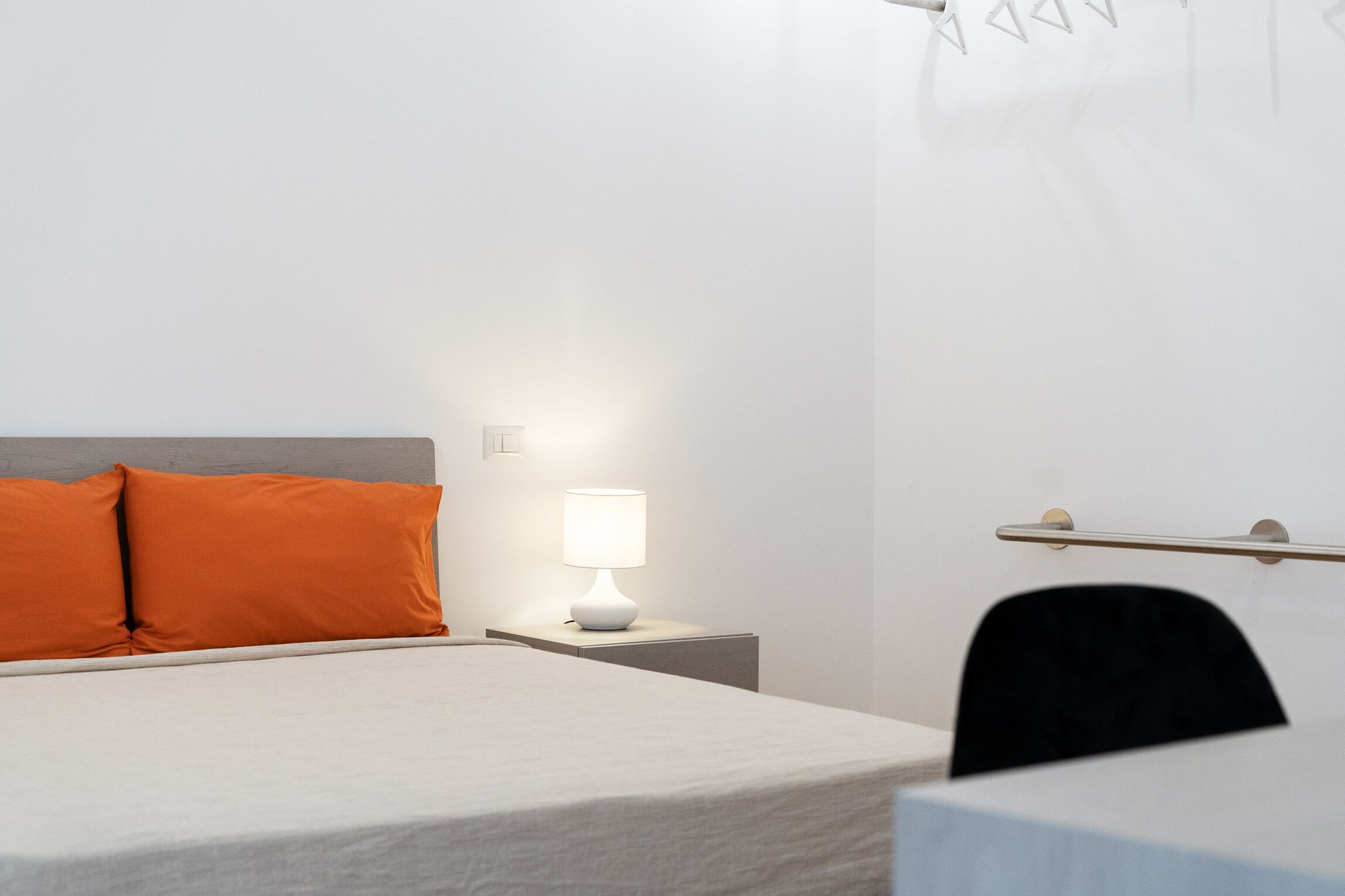 Quarto de hotel com cama, mesa de cabeceira com abajur e uma cadeira.