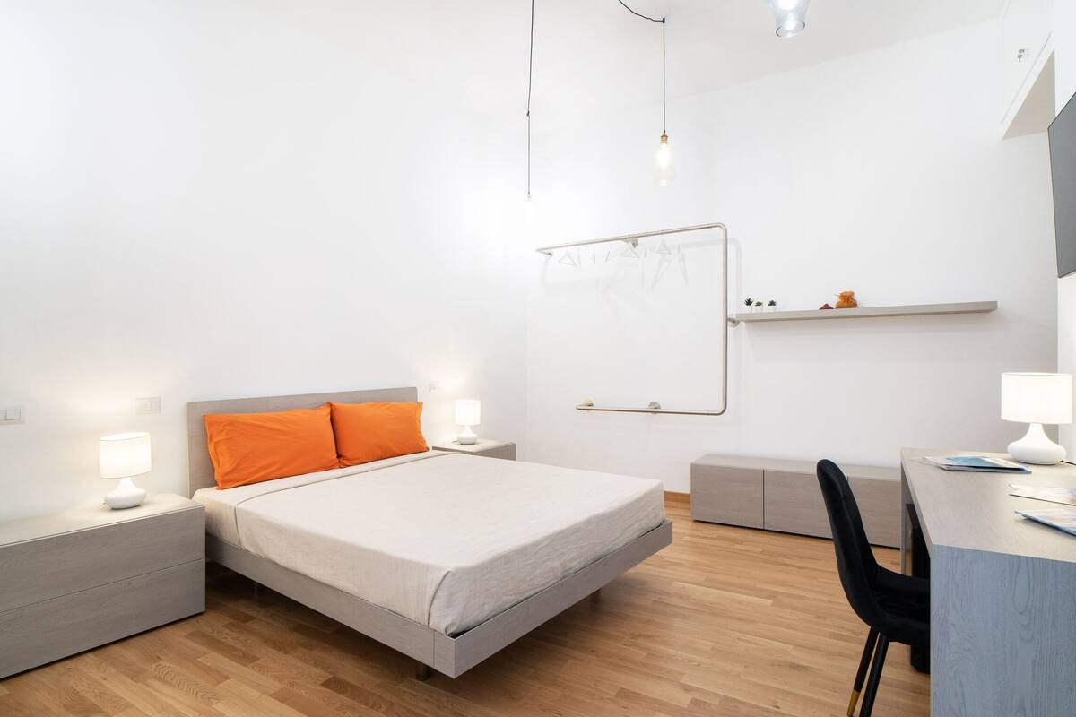 A modern bedroom with a bed, bedside tables, a desk, and a chair.