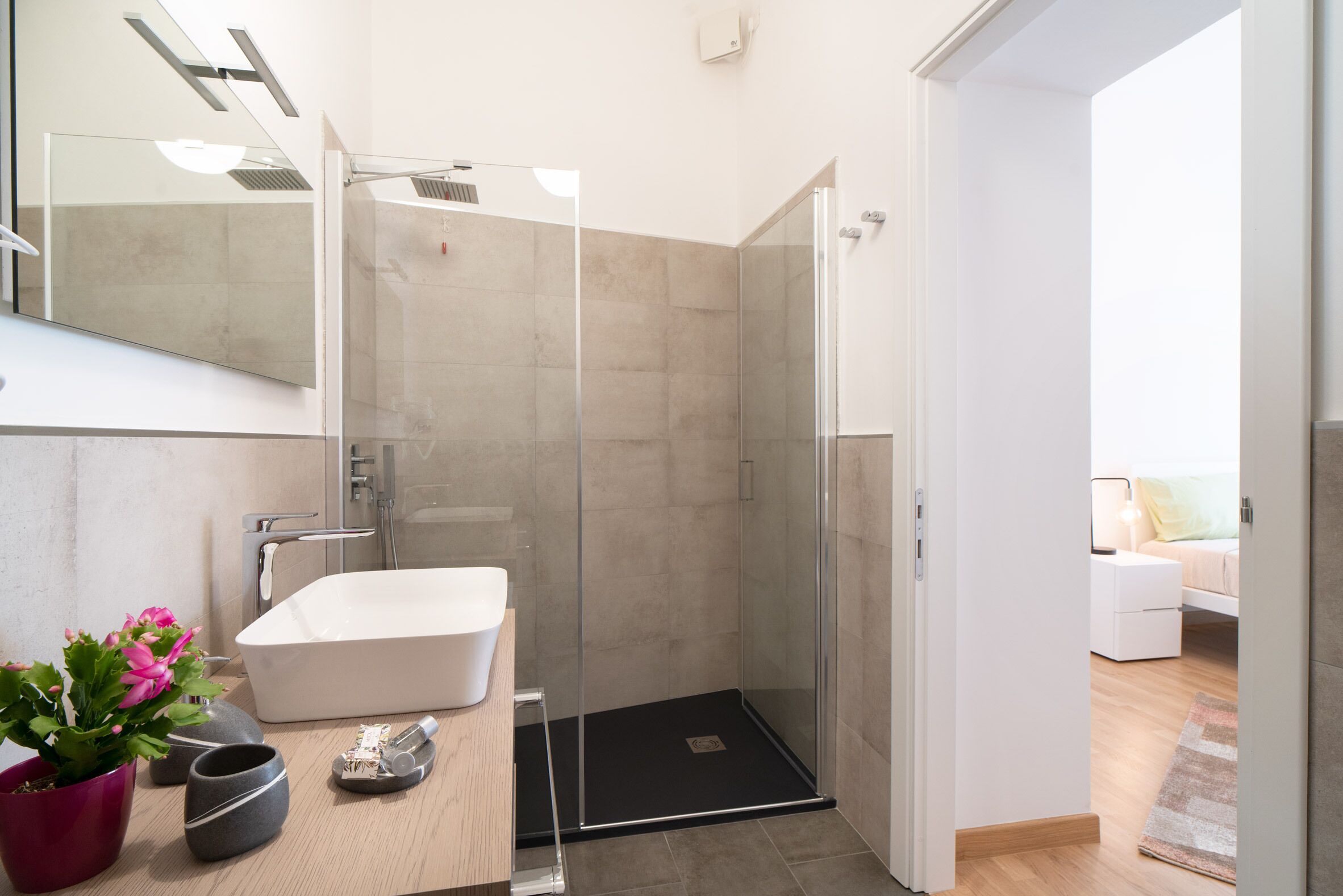 Un bagno moderno con doccia vetrata, lavandino bianco e una pianta in vaso.