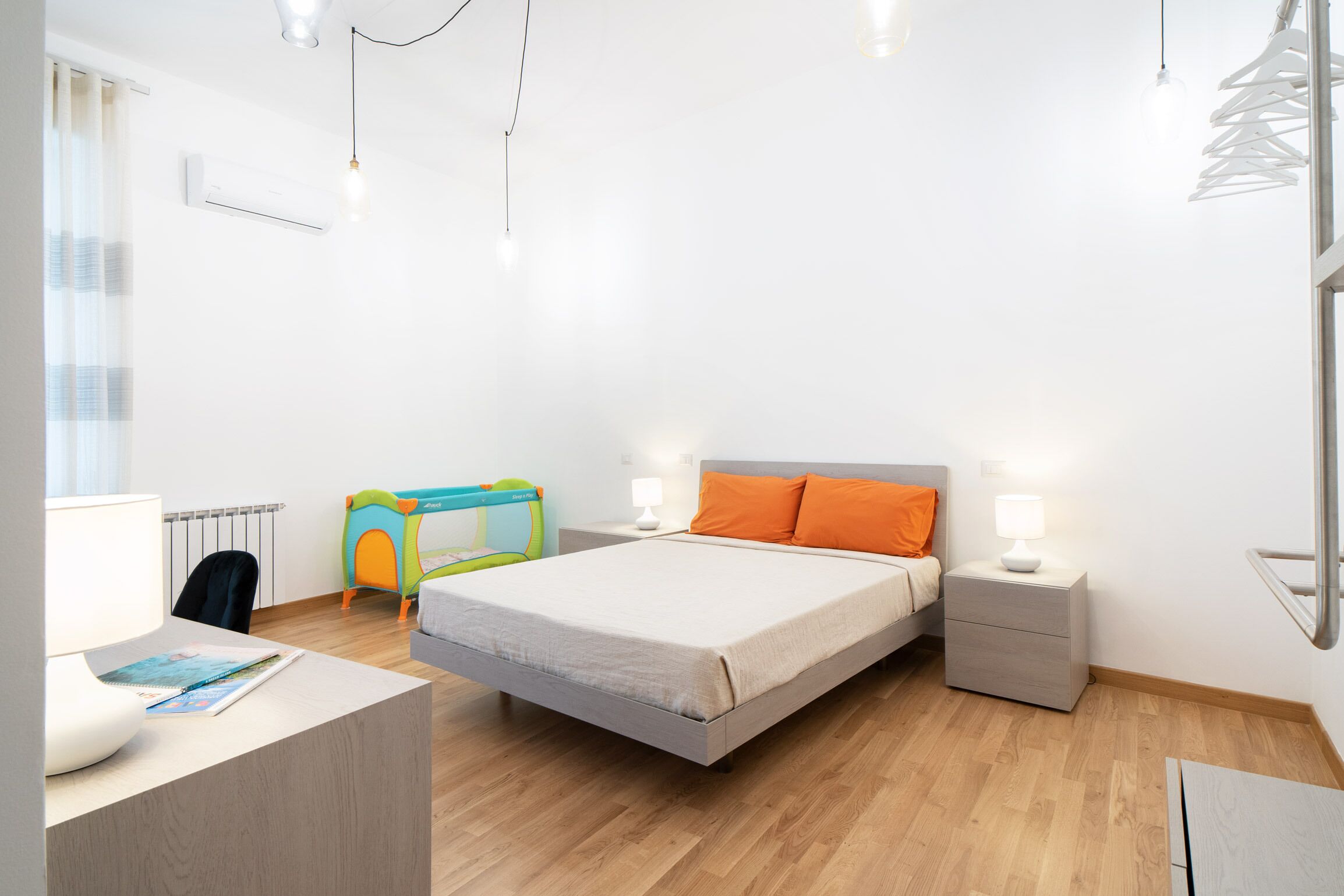 A modern bedroom with a bed, bedside tables, a desk, and a window.