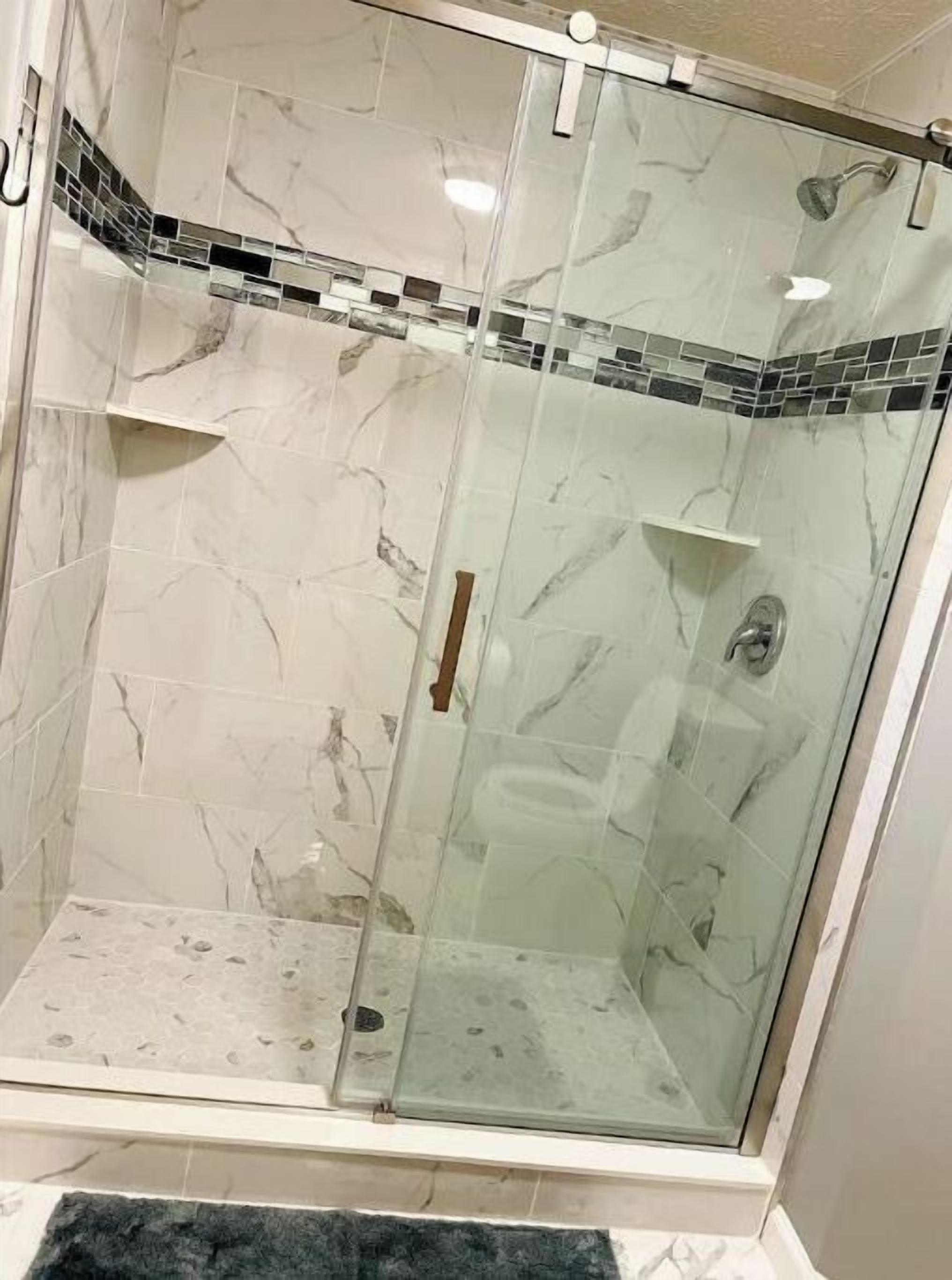 A glass-enclosed shower with a marble wall design and a small shelf.