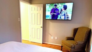 A bedroom with a bed, a television mounted on the wall, and a chair.