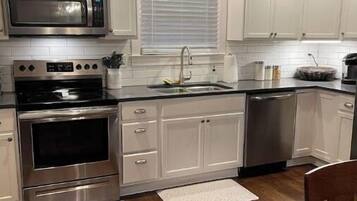 Une cuisine moderne avec des meubles blancs, des appareils en acier inoxydable, un plafond en bois et un coin repas doté d’une table en bois.