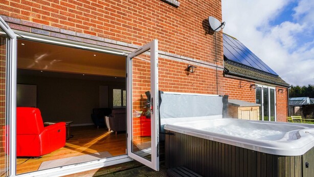 A patio area with a hot tub, a wooden deck, and a brick house. - Unique 5BD Farm House Perfect for Relaxing (Ipswich)