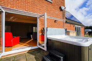A patio area with a hot tub, a wooden deck, and a brick house.