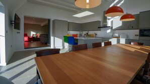 A modern kitchen with a large wooden dining table, red pendant lights, and a view into the living area. - Unique 5BD Farm House Perfect for Relaxing (Ipswich)