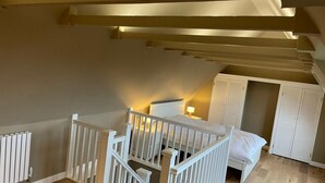 A bedroom with a wooden floor, white bed, and a white crib. There is a radiator on the wall and a staircase leading to another room. - Unique 5BD Farm House Perfect for Relaxing (Ipswich)