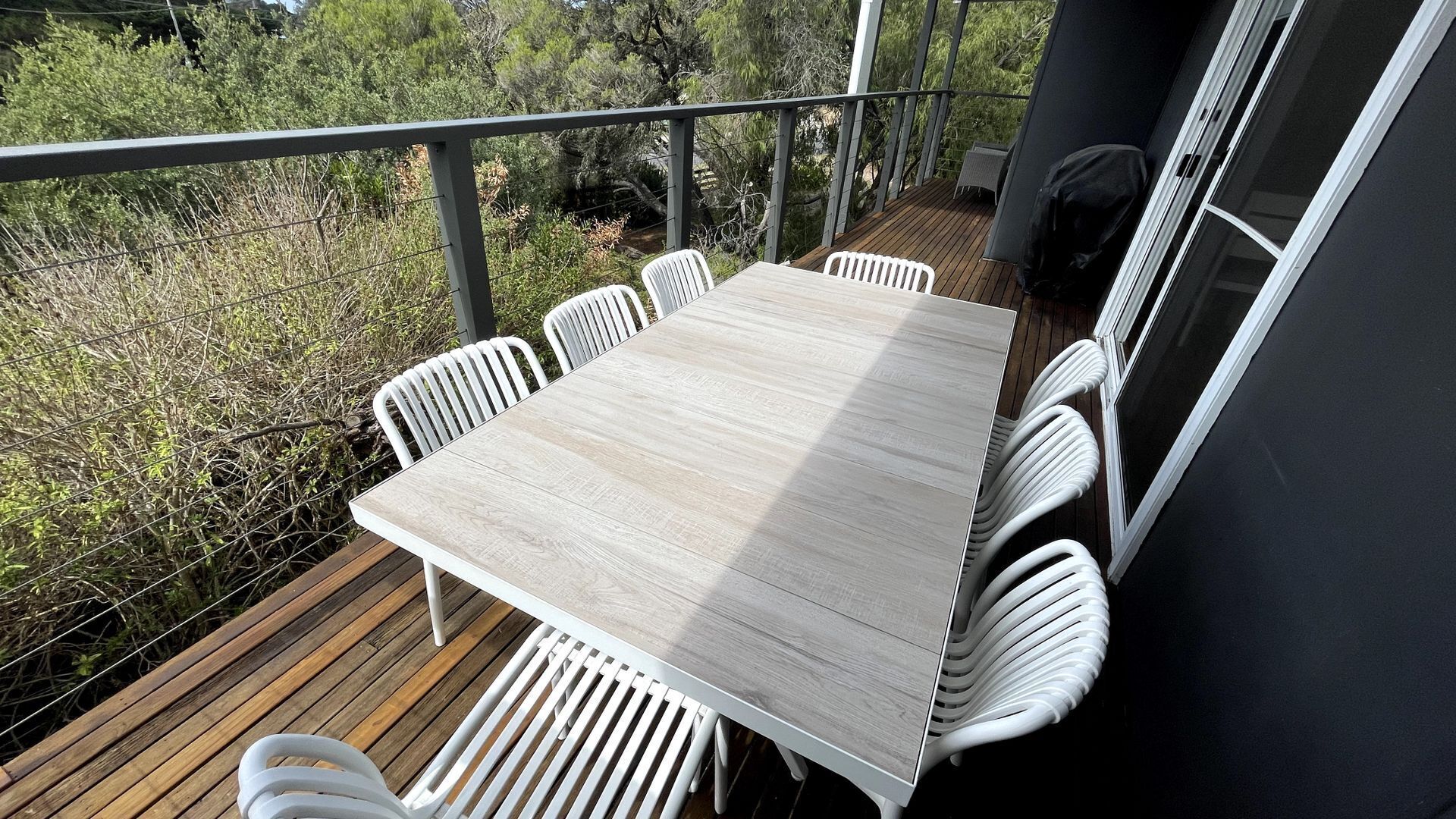 Eine Holzterrasse mit Tisch und Stühlen, umgeben von einer Brüstung und mit Blick auf eine natürliche Landschaft.