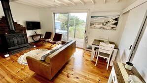 Un salon chaleureux avec un plancher en bois, un canapé, une cheminée et un coin repas comprenant une table et des chaises.