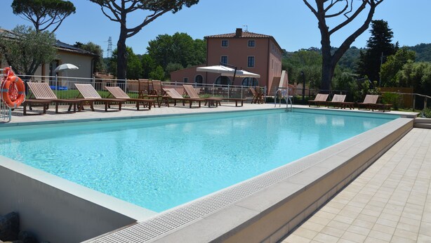 Ein Schwimmbecken mit Liegestühlen und Sonnenschirmen, umgeben von Bäumen und einem Gebäude im Hintergrund.