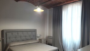 Ein Schlafzimmer mit einem Bett, einem Nachttisch, einer Lampe und einem Fenster mit Vorhängen.