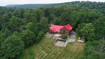 An aerial view of a house with a red roof surrounded by dense forest.
