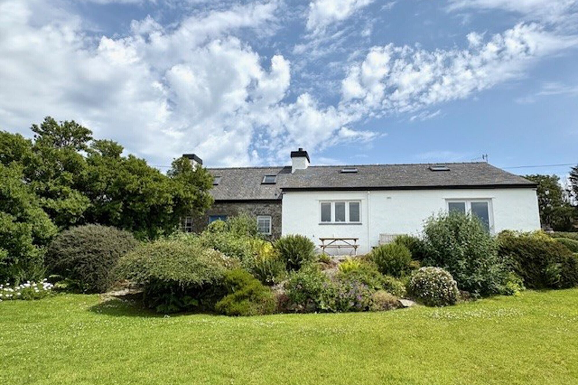 A single-story house with a white exterior, a grey roof, and a small garden in front.