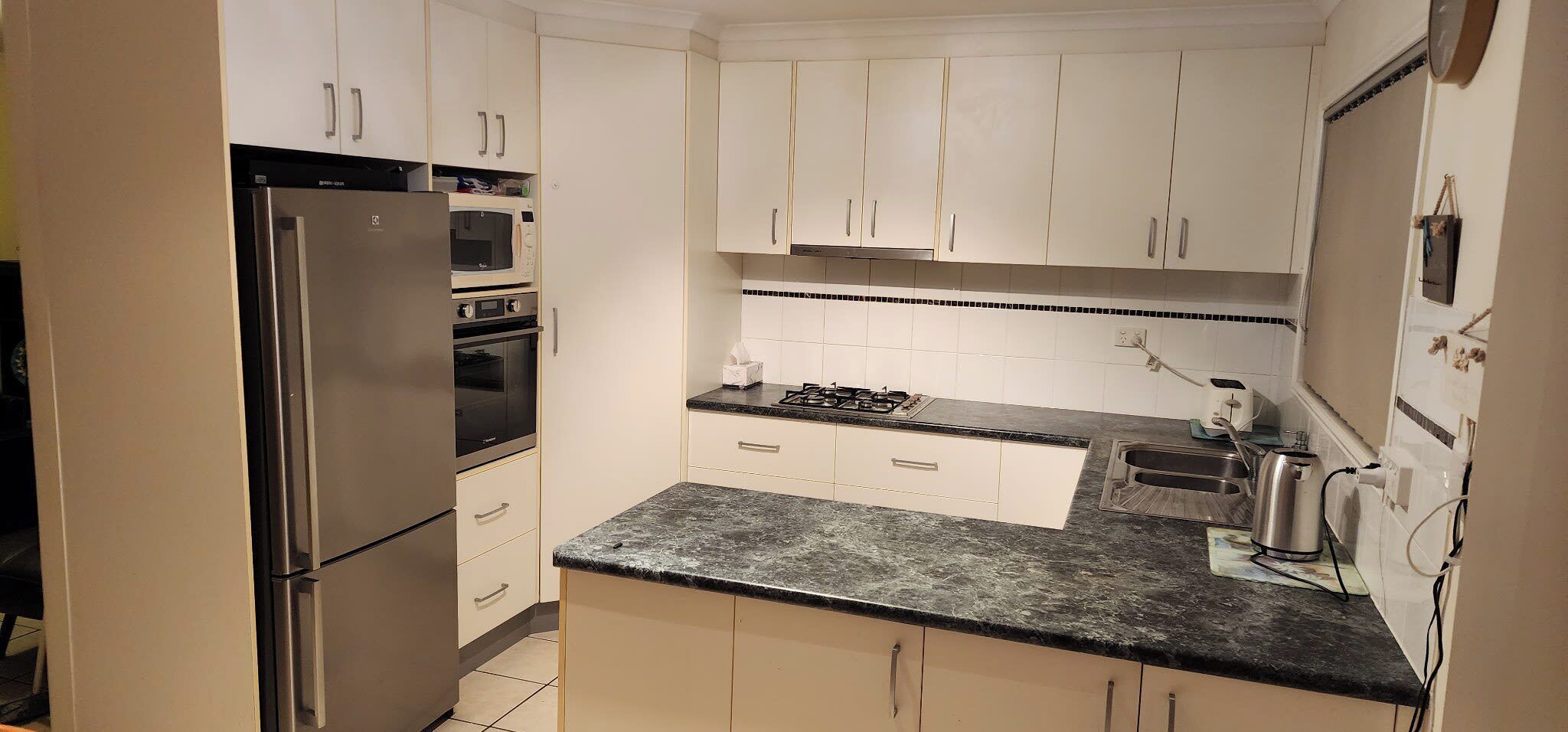 A compact kitchen with white cabinets, a stainless steel refrigerator, a microwave, and a gas stove.