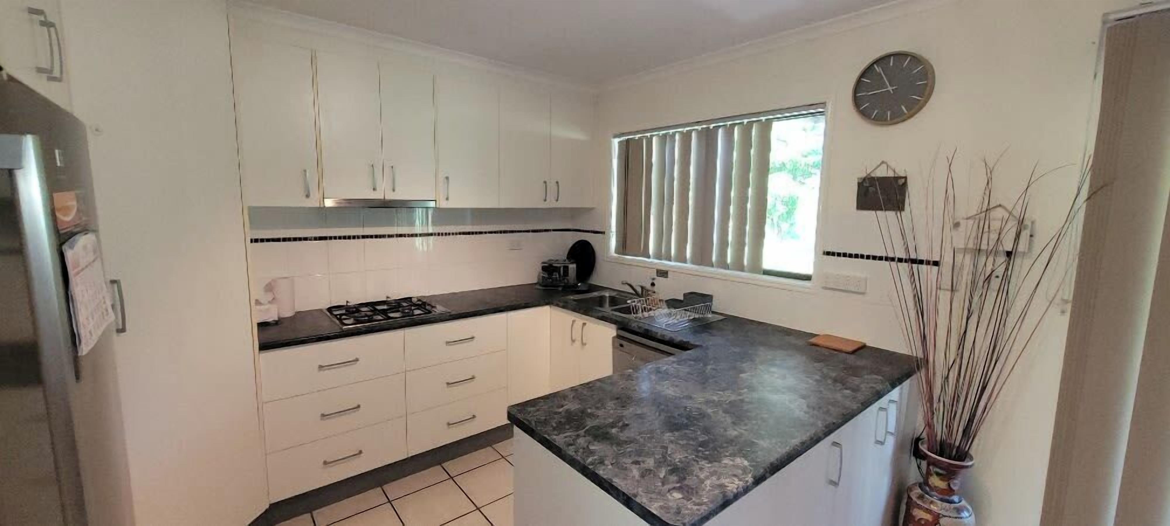 A kitchen with white cabinets, a black countertop, a stove, and a window with blinds.