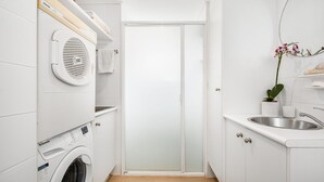 Ein kompakter, moderner Waschraum mit einer Waschmaschine mit Frontlader, einem eingebauten Trockner und einem kleinen Waschbecken.