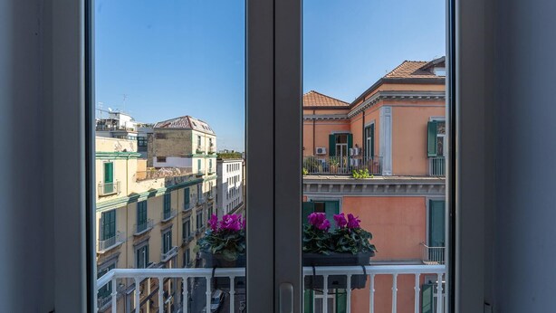 A balcony with a view of a cityscape, featuring buildings with balconies and a clear sky.