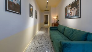 A hallway with a green sofa, framed artwork, and a lamp.