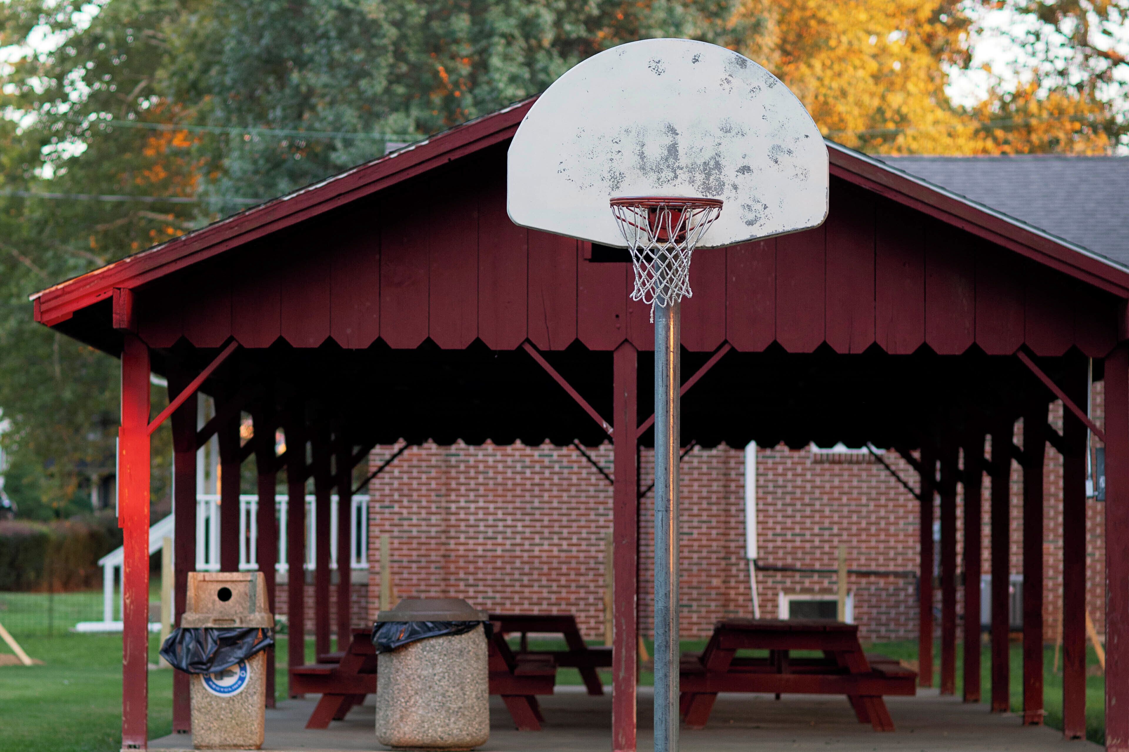 A covered pavilion with a basketball hoop, picnic tables, and a trash can.