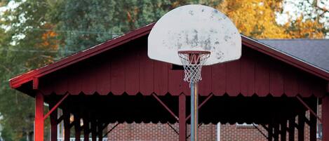 A covered pavilion with a basketball hoop, picnic tables, and a trash can.