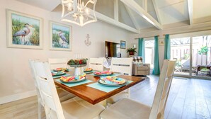 A dining area with a wooden table set for four, white chairs, and a chandelier. - Community Perks! Sunny Hilton Head Island Retreat (Hilton Head Island)