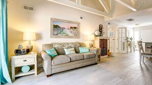 A living room with a beige sofa, a painting, a lamp, a bookshelf, and a dining area visible in the background. - Community Perks! Sunny Hilton Head Island Retreat (Hilton Head Island)