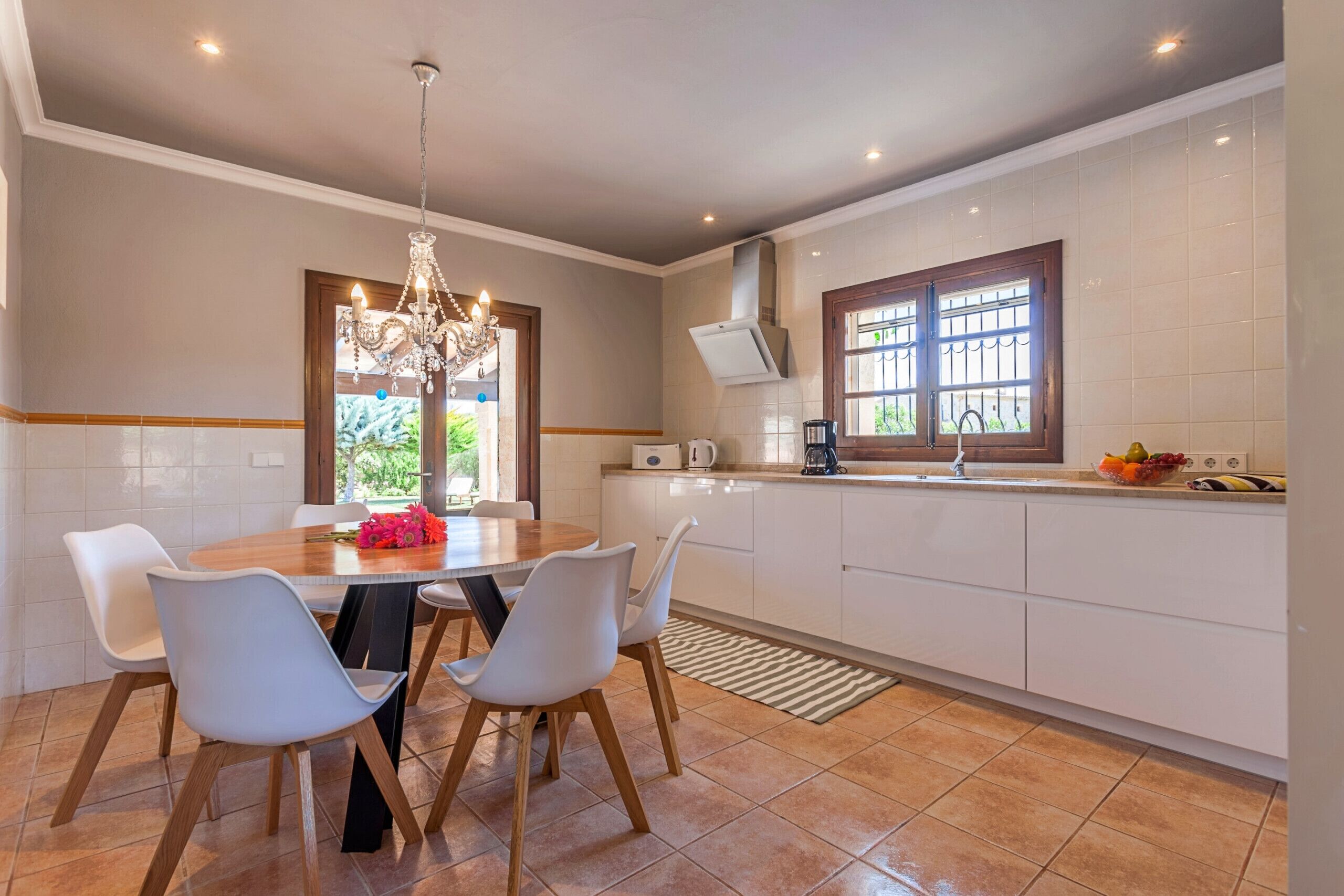 Une cuisine moderne avec des meubles blancs, un lustre et un coin repas comprenant une table et des chaises.