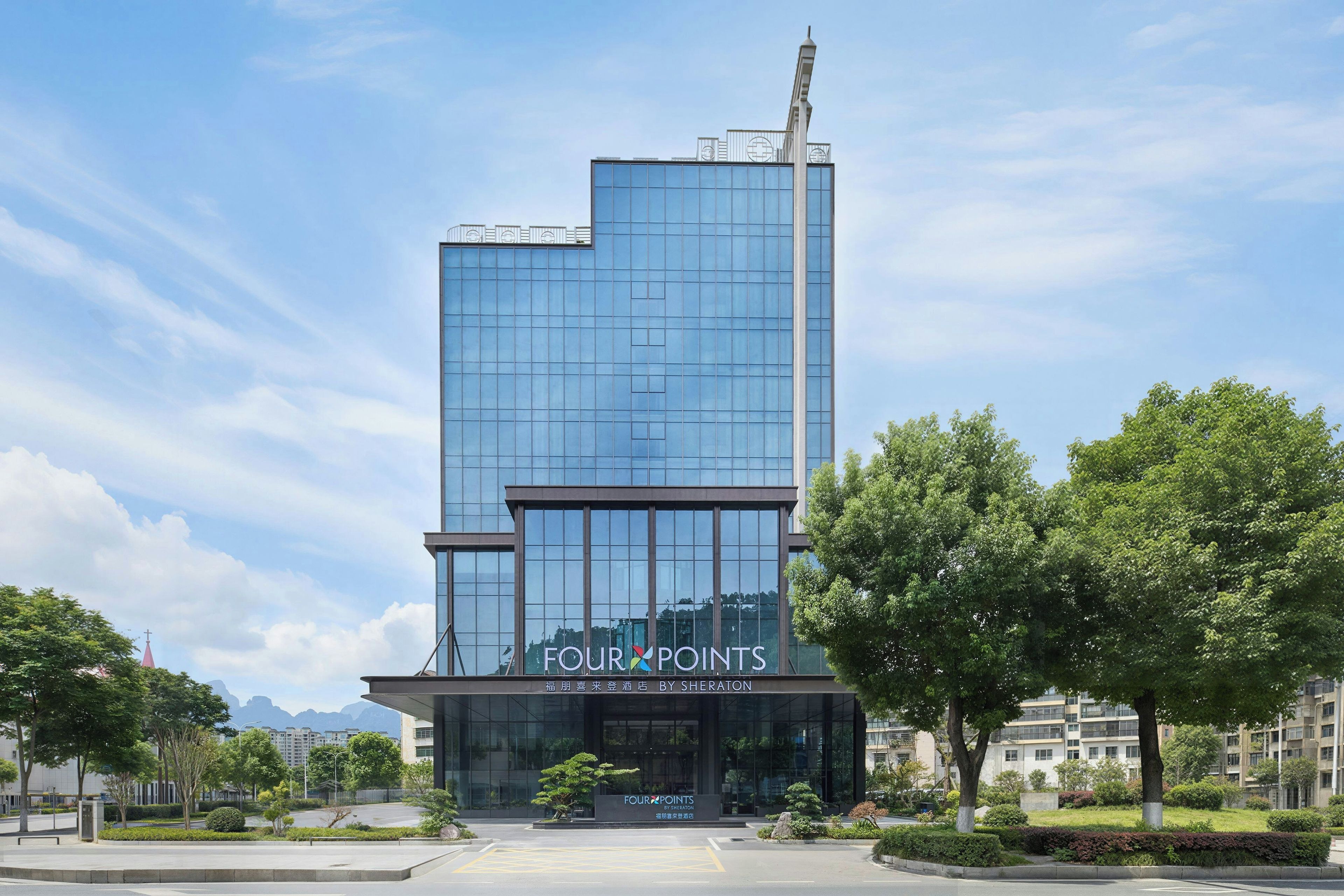 A modern hotel building with a glass facade and signage for 'FOUR POINTS BY SHERATON'.