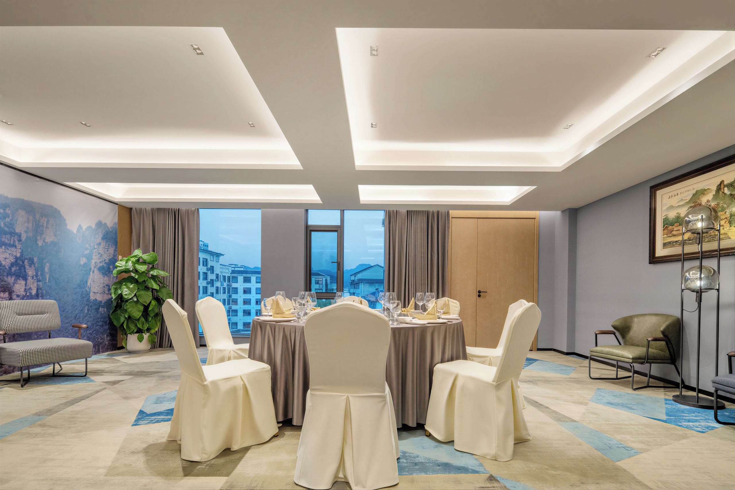 Un salón de conferencias con una mesa redonda, cuatro sillas y vistas a edificios a través de amplios ventanales.