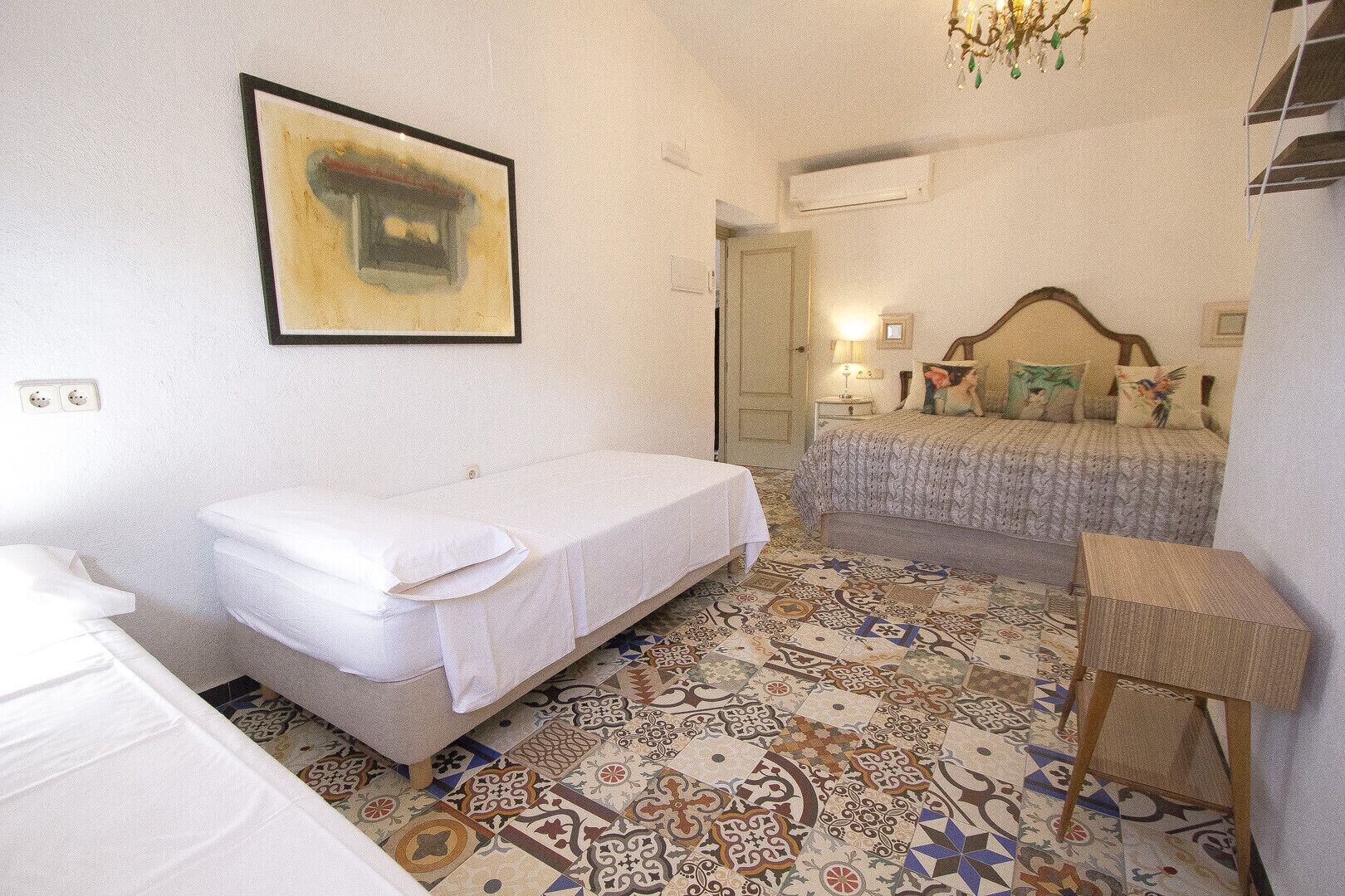 Un dormitorio con cama, mesita de noche, silla, piso con diseño y un cuadro en la pared.