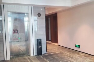 Un vestíbulo de hotel con un ascensor de vidrio, una recepción e indicaciones.
