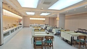 Un comedor amplio con varias mesas y sillas, una barra larga con vitrinas y un techo alto con tragaluces.