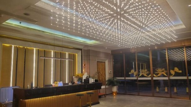 Zona de recepción de un hotel con diseño moderno, que incluye mostrador de recepción, área de estar y un aplique decorativo en el techo.