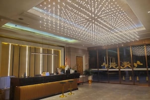Un hall de hotel con mostrador de recepción, una instalación de luces en el techo y una puerta de cristal grande con detalles dorados.