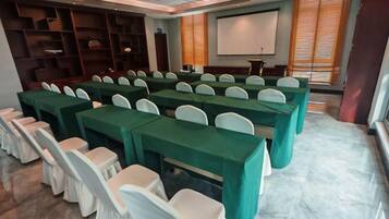 A conference room with rows of tables and chairs, a projector screen, and a presentation area.