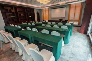 A conference room with rows of tables and chairs, a projector screen, and a presentation area.